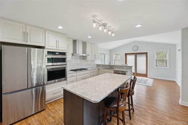 3395 W Maple Rd, Wixom, MI 48393 - kitchen featuring appliances with stainless steel finishes, wall chimney exhaust hood, a peninsula, vaulted ceiling, and light wood-style flooring