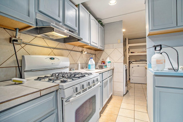 11303 W Dr N, Bellevue, MI 49021 - kitchen with white gas range oven, washer / clothes dryer, light countertops, light tile patterned flooring, and under cabinet range hood