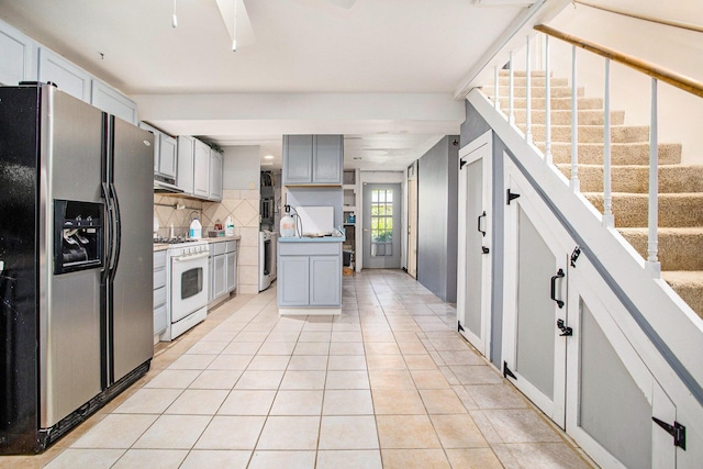 11303 W Dr N, Bellevue, MI 49021 - kitchen featuring stainless steel refrigerator with ice dispenser, white gas range oven, light tile patterned floors, gray cabinetry, and decorative backsplash