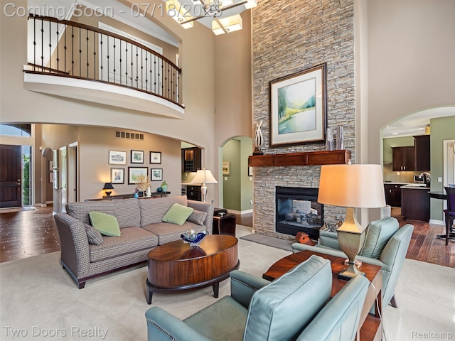 3551 Royal Berkshire Ln, Oakland, MI 48363 - living room featuring arched walkways, a towering ceiling, a chandelier, a fireplace, and wood finished floors