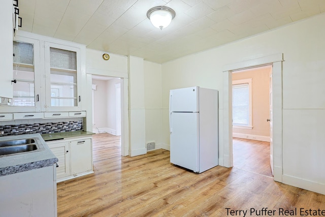 2550 Crozier Ave, Muskegon, MI 49441 - kitchen with freestanding refrigerator, light wood-type flooring, white cabinets, backsplash, and glass insert cabinets