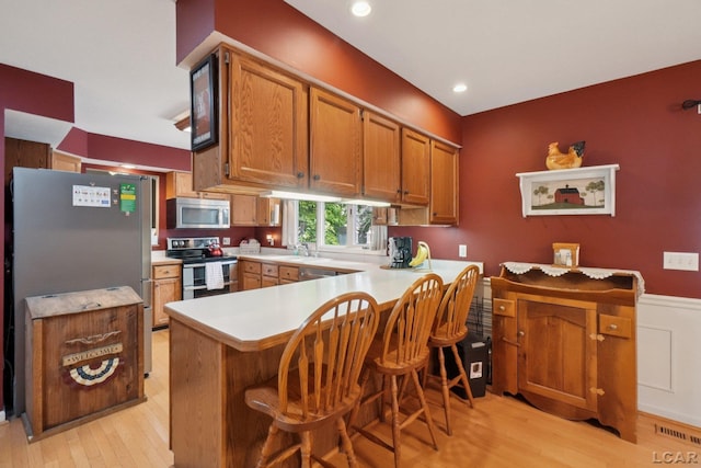 221 Burt St, Tecumseh, MI 49286 - kitchen featuring appliances with stainless steel finishes, a peninsula, light countertops, light wood-type flooring, and wainscoting
