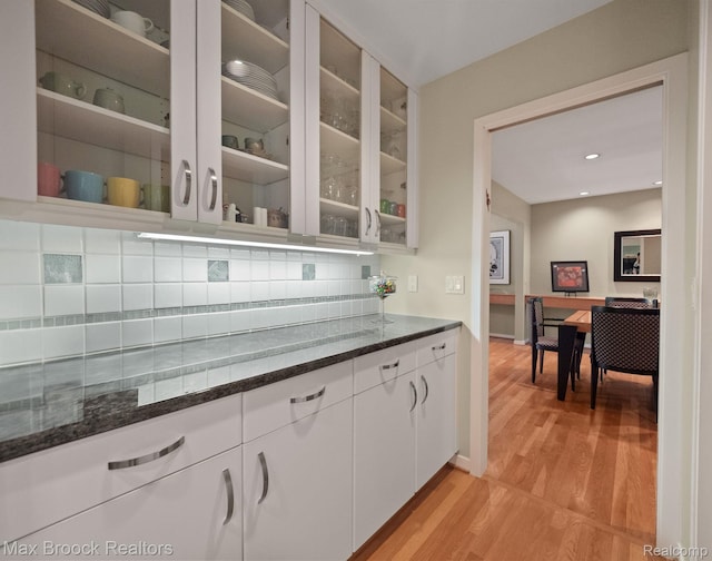 6224 Bromley Ct, West Bloomfield, MI 48322 - kitchen featuring dark stone counters, backsplash, glass insert cabinets, light wood-style flooring, and white cabinetry