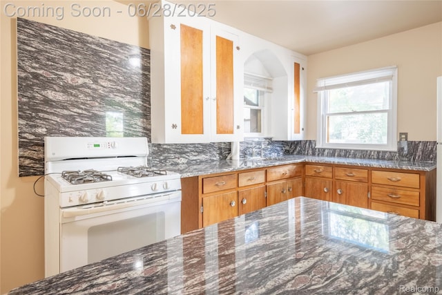 785 Kenilworth Ave, Pontiac, MI 48340 - kitchen featuring white gas range oven, dark stone countertops, brown cabinets, and arched walkways