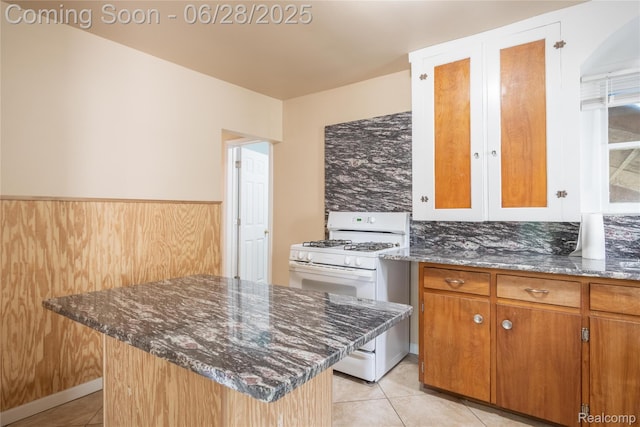 785 Kenilworth Ave, Pontiac, MI 48340 - kitchen with white range with gas cooktop, light tile patterned floors, dark stone countertops, a center island, and brown cabinets
