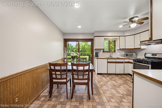 3123 W Utica Rd, Shelby Twp, MI 48317 - kitchen with stainless steel gas range, white cabinetry, ceiling fan, a wainscoted wall, and under cabinet range hood