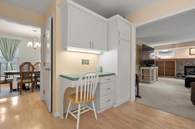 220 Deer Path Ln, Battle Creek, MI 49015 - kitchen with light wood finished floors, white cabinetry, a brick fireplace, a chandelier, and a desk