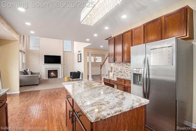 27455 Harrington Way, Novi, MI 48374 - kitchen featuring stainless steel fridge, a lit fireplace, light wood-style flooring, brown cabinetry, and light stone counters