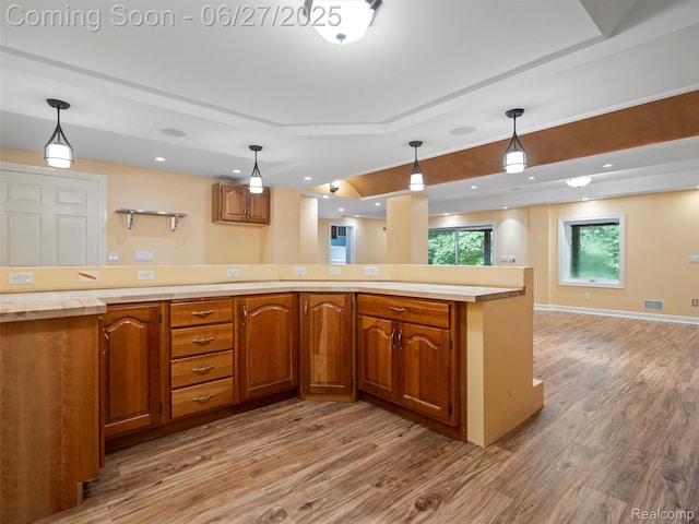 9767 Whisperwood Ln, Brighton, MI 48116 - kitchen featuring a raised ceiling, light wood finished floors, open floor plan, brown cabinets, and light countertops