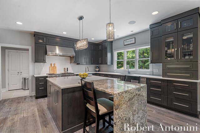 1977 Emerald Glen Ct NE, Ada, MI 49301 - kitchen with ventilation hood, light wood-style floors, a center island, glass insert cabinets, and recessed lighting
