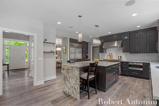 1977 Emerald Glen Ct NE, Ada, MI 49301 - kitchen featuring premium appliances, ventilation hood, wood finished floors, a center island with sink, and decorative backsplash
