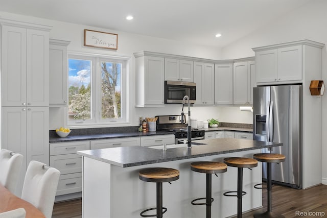 619 N Watkins, Perry, MI 48872 - kitchen with stainless steel appliances, dark countertops, an island with sink, a breakfast bar, and dark wood-style flooring