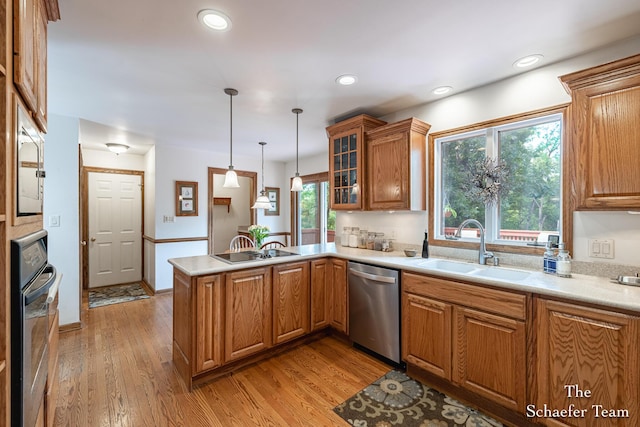 175 Honey Creek Ave NE, Ada, MI 49301 - kitchen with stainless steel appliances, a peninsula, brown cabinetry, decorative light fixtures, and light wood finished floors
