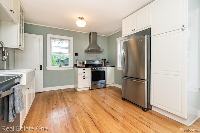 1388 W Troy St, Ferndale, MI 48220 - kitchen featuring appliances with stainless steel finishes, wall chimney exhaust hood, white cabinets, light wood-style flooring, and ornamental molding