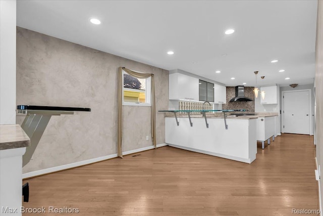 2222 Garland St, Sylvan Lake, MI 48320 - kitchen featuring wall chimney exhaust hood, white cabinets, light wood-style floors, a peninsula, and recessed lighting