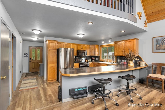 17318 Thunder Bay Ct, Howard City, MI 49329 - kitchen with stainless steel appliances, a peninsula, light wood finished floors, a kitchen bar, and brown cabinets