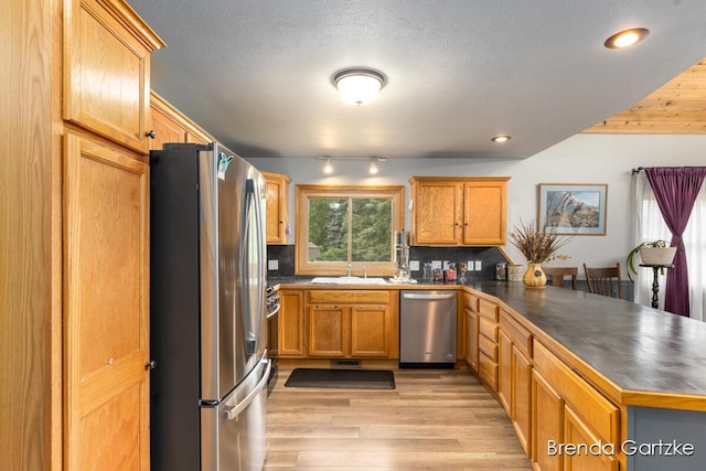 17318 Thunder Bay Ct, Howard City, MI 49329 - kitchen with stainless steel appliances, a peninsula, light wood-type flooring, dark countertops, and backsplash