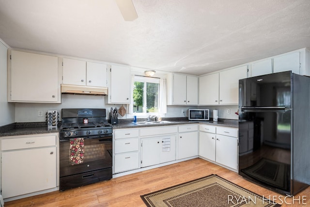 160 Division St, Saranac, MI 48881 - kitchen with black appliances, under cabinet range hood, dark countertops, light wood finished floors, and white cabinetry