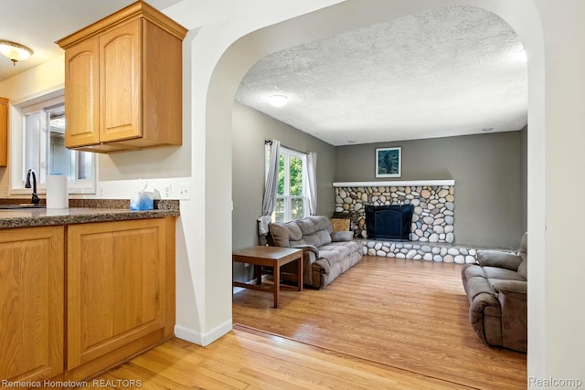 42424 Bradner Ct, Plymouth, MI 48170 - living room featuring arched walkways, light wood-style floors, a stone fireplace, and a textured ceiling