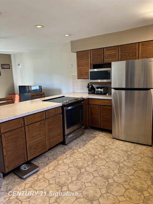 11424 Hazel Ave, Grand Blanc, MI 48439 - kitchen with appliances with stainless steel finishes, tile countertops, brown cabinetry, recessed lighting, and decorative backsplash