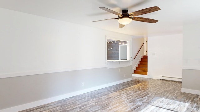 11427 Colonial Woods Dr, Clio, MI 48420 - spare room featuring a baseboard heating unit, stairway, a ceiling fan, and wood finished floors