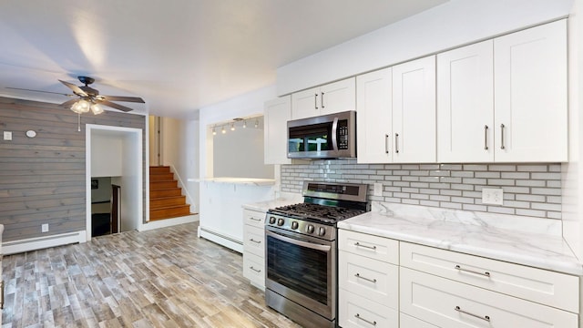11427 Colonial Woods Dr, Clio, MI 48420 - kitchen featuring appliances with stainless steel finishes, a baseboard radiator, decorative backsplash, light wood-style flooring, and wooden walls