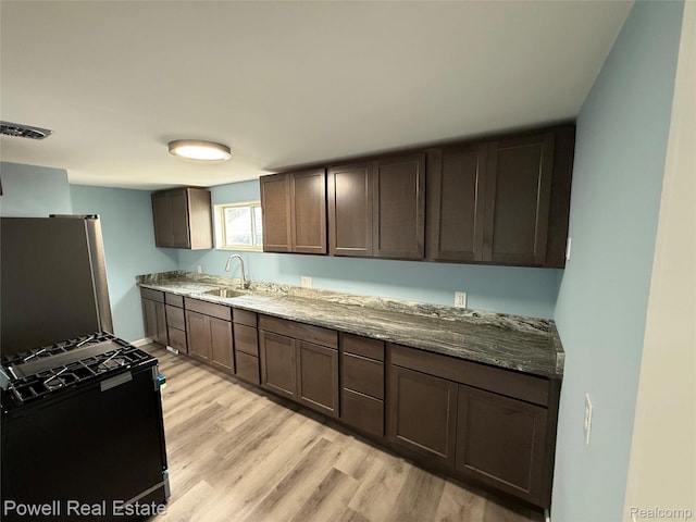 2326 Silver Cir, Pontiac, MI 48328 - kitchen with freestanding refrigerator, black range with gas stovetop, light wood finished floors, stone countertops, and dark brown cabinets