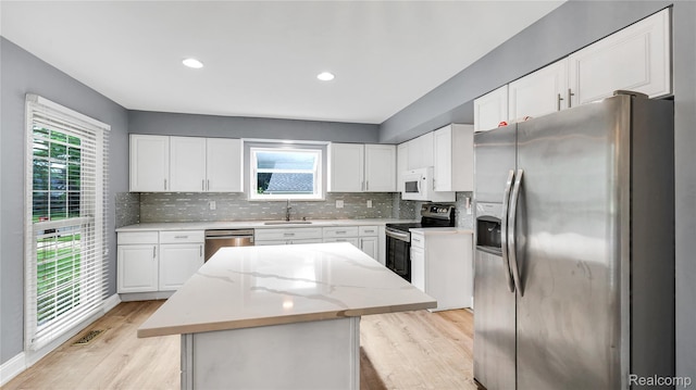 6596 Corral Ct, West Bloomfield, MI 48324 - kitchen with stainless steel appliances, a center island, light wood finished floors, decorative backsplash, and white cabinets