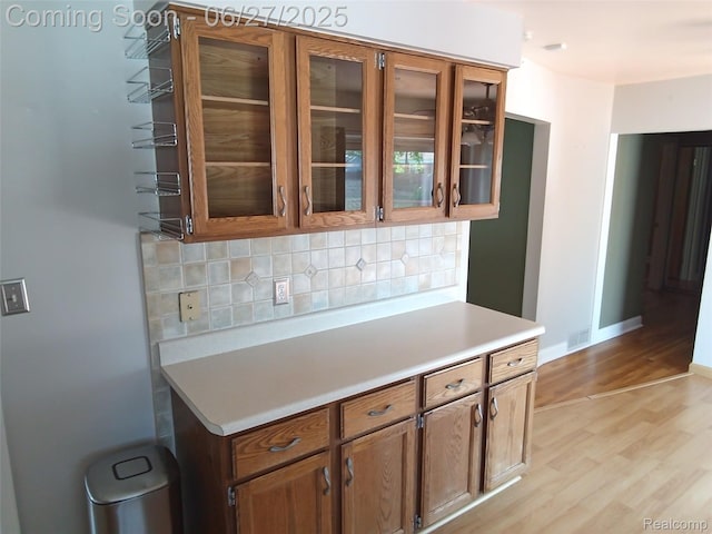 8283 Christine St, Warren, MI 48093 - kitchen featuring light wood finished floors, decorative backsplash, light countertops, glass insert cabinets, and brown cabinets