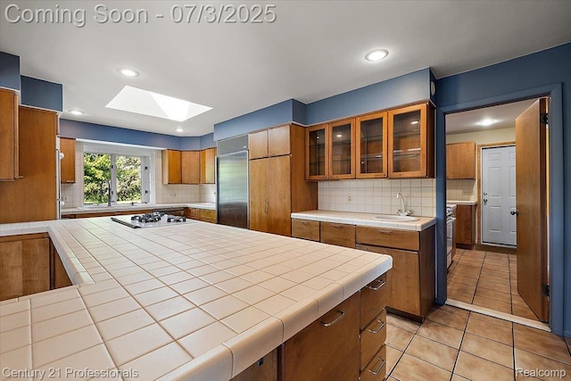 291 N Baldwin Rd, Clarkston, MI 48348 - kitchen with stainless steel built in fridge, a skylight, tile counters, brown cabinetry, and gas stovetop