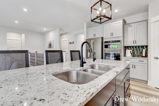 8205 Autumn Acres Dr, Rockford, MI 49341 - kitchen featuring stainless steel double oven, light stone counters, hanging light fixtures, light wood finished floors, and a chandelier