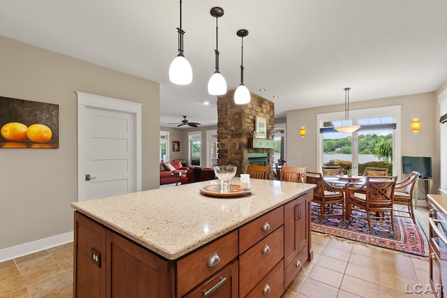 14967 S Shore Dr, Addison, MI 49220 - kitchen with a stone fireplace, ceiling fan, pendant lighting, light stone countertops, and a center island