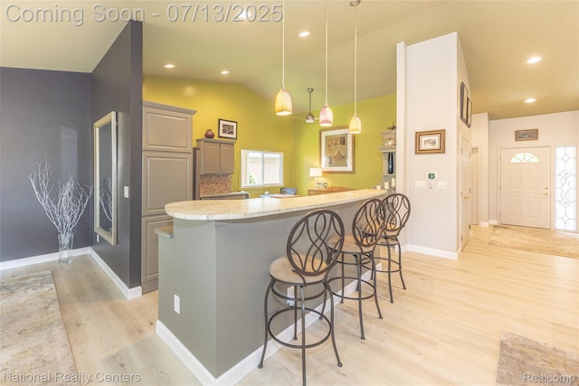 285 Ash Ct, South Lyon, MI 48178 - kitchen with light wood-style flooring, a breakfast bar, vaulted ceiling, gray cabinetry, and pendant lighting