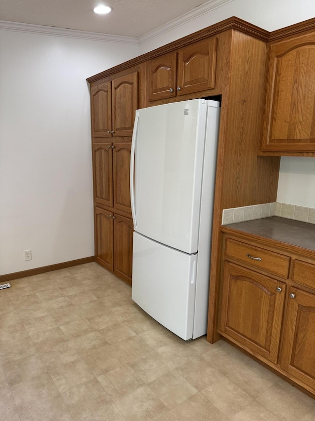 8484 Zosel St, Onekama, MI 49675 - kitchen with freestanding refrigerator, brown cabinets, crown molding, dark countertops, and recessed lighting