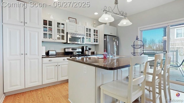 229 Huron St, South Haven, MI 49090 - kitchen with stainless steel appliances, light wood-type flooring, a kitchen breakfast bar, a center island with sink, and white cabinets