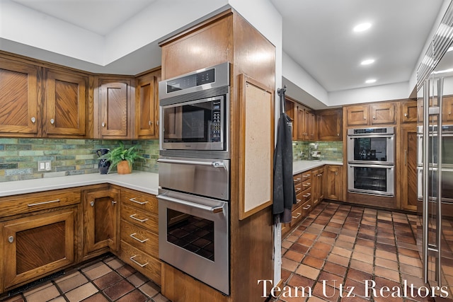 410 Greentree Ln NE, Ada, MI 49301 - kitchen featuring stainless steel appliances, brown cabinetry, decorative backsplash, light countertops, and recessed lighting