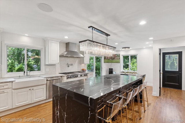 4438 Stony River Dr, Bloomfield Hills, MI 48301 - kitchen with wall chimney range hood, appliances with stainless steel finishes, light stone counters, white cabinets, and light wood finished floors
