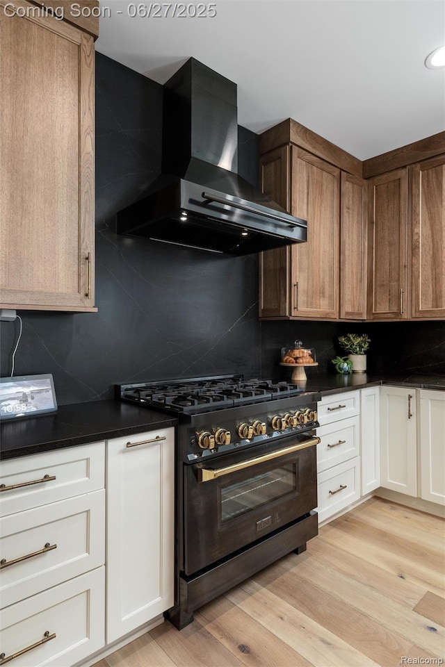 8264 Stoney Creek Dr, South Lyon, MI 48178 - kitchen with gas stove, wall chimney range hood, dark countertops, backsplash, and light wood-style flooring