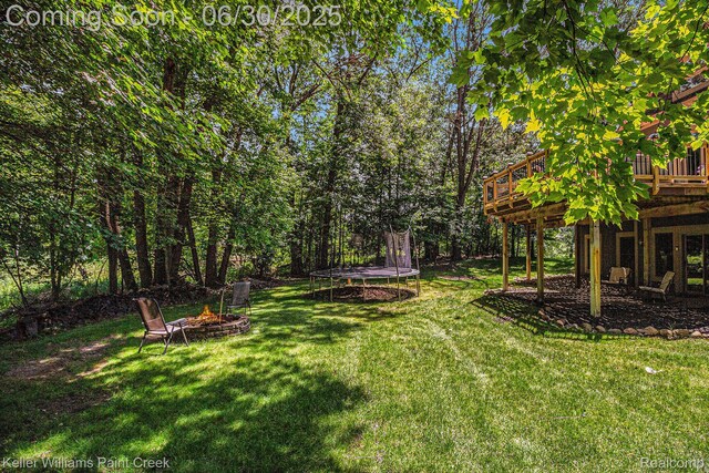2868 Masters Ct, Pinckney, MI 48169 - view of grassy yard featuring a trampoline, a fire pit, and a deck