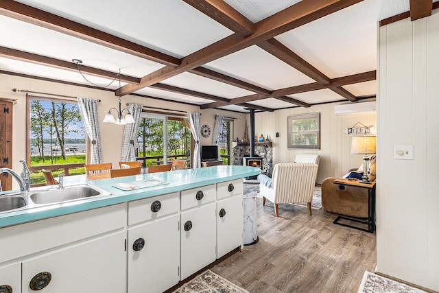 5510 W Lattin Rd, Pentwater, MI 49449 - kitchen with a wood stove, light wood-type flooring, a chandelier, beamed ceiling, and white cabinets