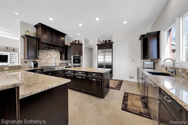 5001 Forest Vly, Clarkston, MI 48348 - kitchen featuring appliances with stainless steel finishes, tasteful backsplash, light stone counters, dark brown cabinetry, and premium range hood