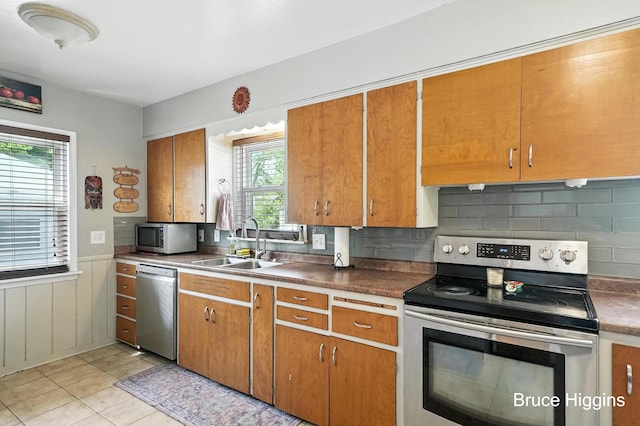 920 Graceland St NE, Grand Rapids, MI 49505 - kitchen with stainless steel appliances, brown cabinetry, wainscoting, decorative backsplash, and light tile patterned flooring