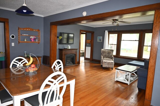 2245 Morton Ave, Muskegon, MI 49441 - dining space with wood finished floors, a fireplace, a ceiling fan, crown molding, and a textured ceiling