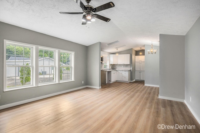 6973 W Blue Water Hwy, Saranac, MI 48881 - unfurnished living room featuring light wood-style flooring, a ceiling fan, lofted ceiling, a chandelier, and a textured ceiling