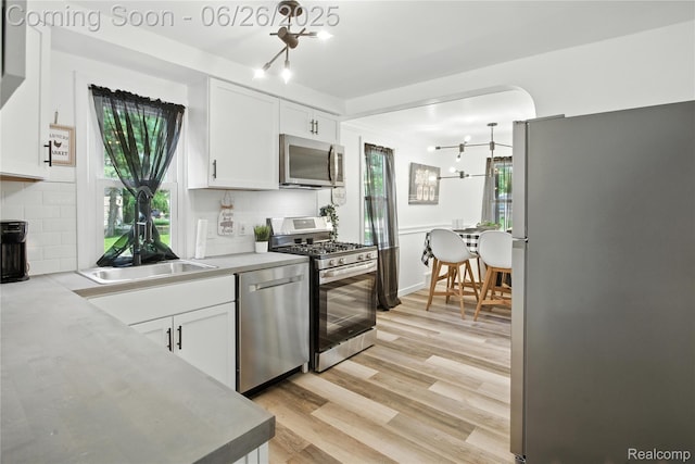 8411 Hugh St, Westland, MI 48185 - kitchen with stainless steel appliances, white cabinets, tasteful backsplash, light wood-style flooring, and a chandelier