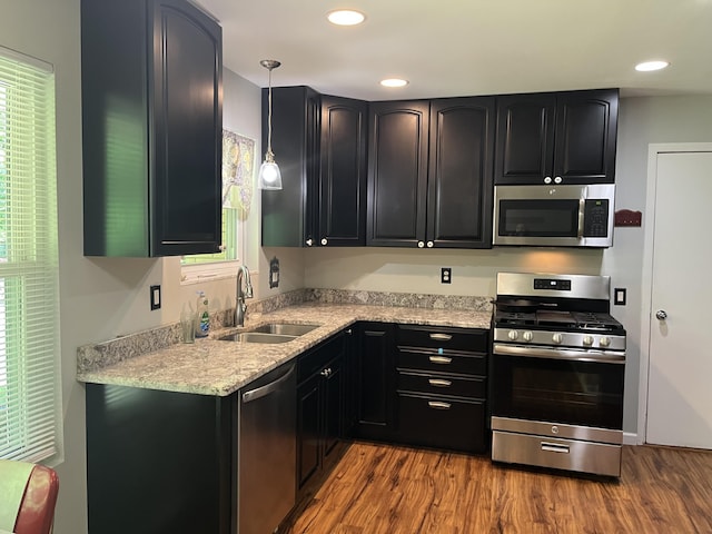 810 Oakgrove, Highland, MI 48356 - kitchen featuring stainless steel appliances, wood finished floors, dark cabinets, hanging light fixtures, and light stone countertops