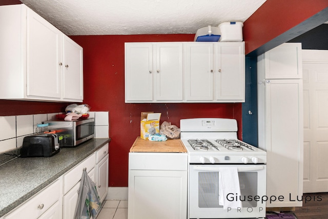 612 Norman St, Lansing, MI 48910 - kitchen with white gas range, white cabinetry, stainless steel microwave, a textured ceiling, and light tile patterned flooring