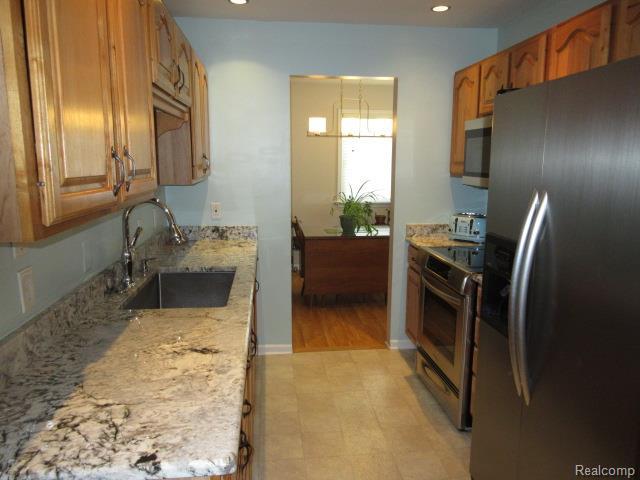 3521 Brandt Ln, Metamora, MI 48455 - kitchen with stainless steel appliances, recessed lighting, brown cabinetry, a chandelier, and light stone counters