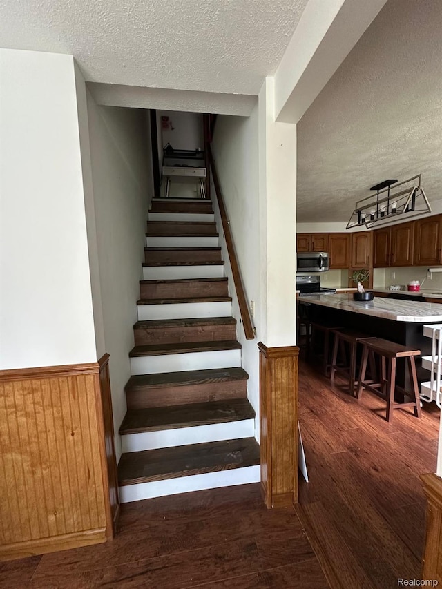 4502 E Wilkinson Rd, Owosso, MI 48867 - stairway with a textured ceiling, wood finished floors, and a wainscoted wall