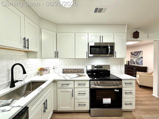 2526 Genes Dr, West Bloomfield, MI 48326 - kitchen featuring appliances with stainless steel finishes, light stone counters, backsplash, light wood-type flooring, and white cabinets